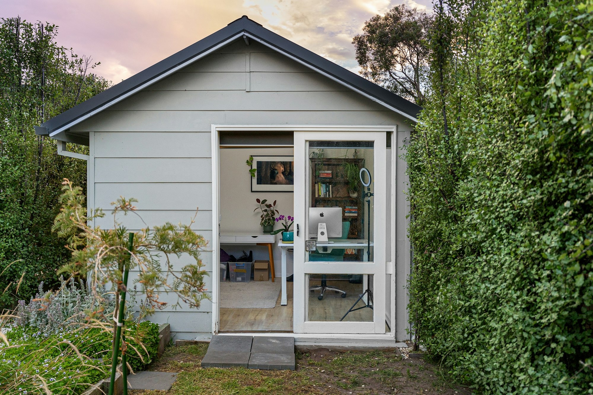 Small grey-sided backyard suite with a glass door, between garden hedges